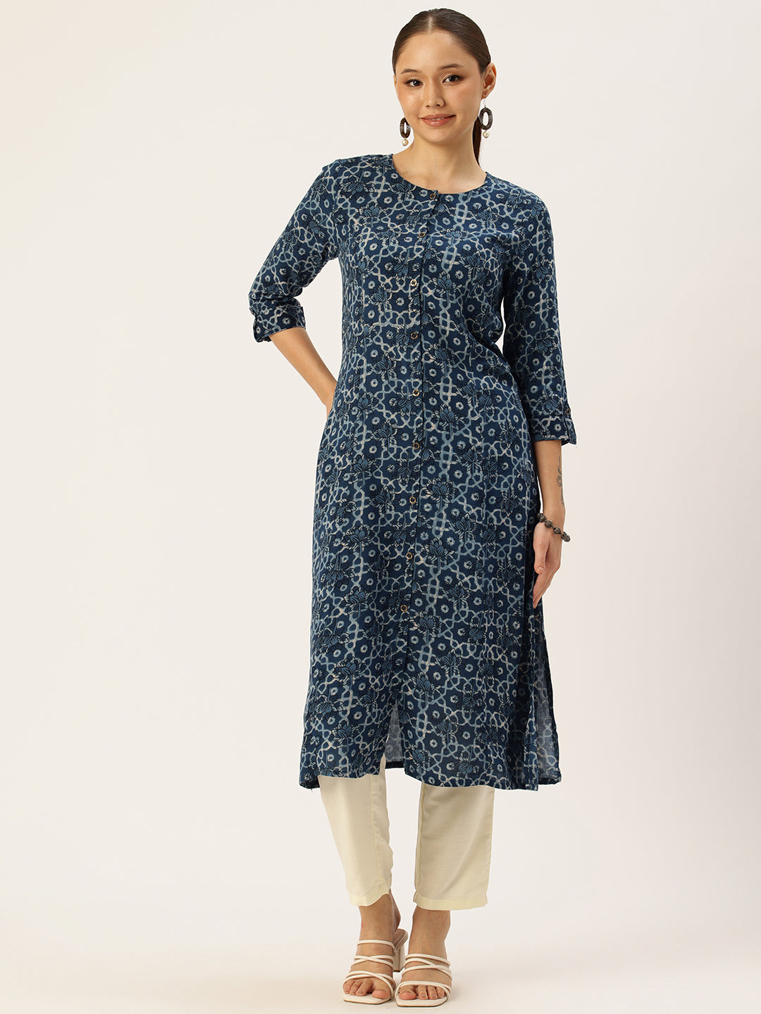 A woman standing and posing in a blue geometric printed kurta with 3/4 sleeves, paired with light pants and carrying a beige purse. Blue Geometric Printed Kurta, Princess Cur Kurta, A-Line Kurta, Floral Print, Mandarin Collar kurta, printed kurta